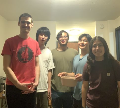 A group of young adults gathered for a potluck dinner in a dorm room.